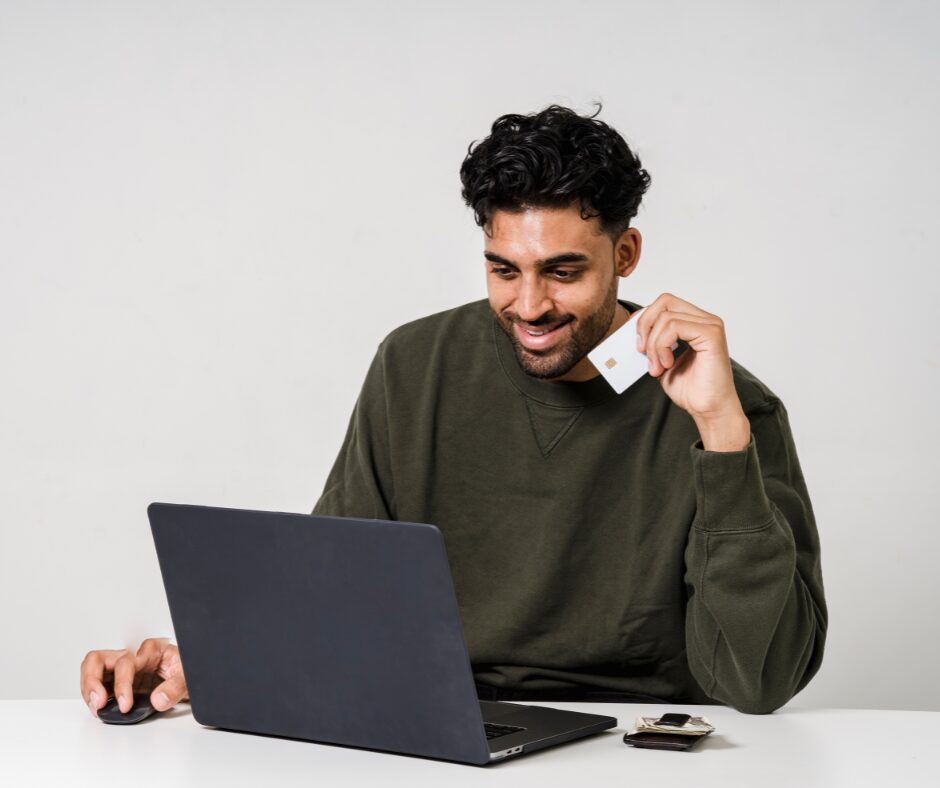 Man holding a credit card while in front of a laptop.