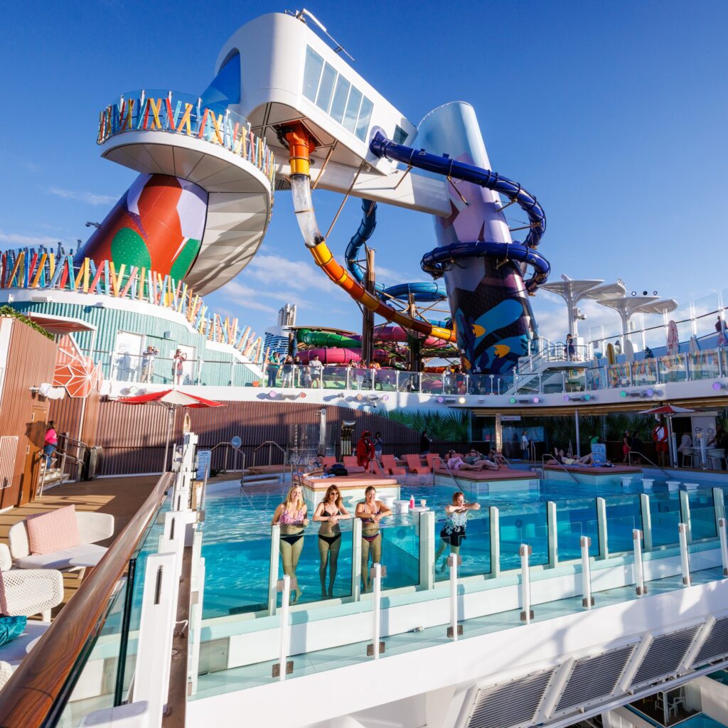 People on the pool area of Icon of the Seas with water slide on the background.