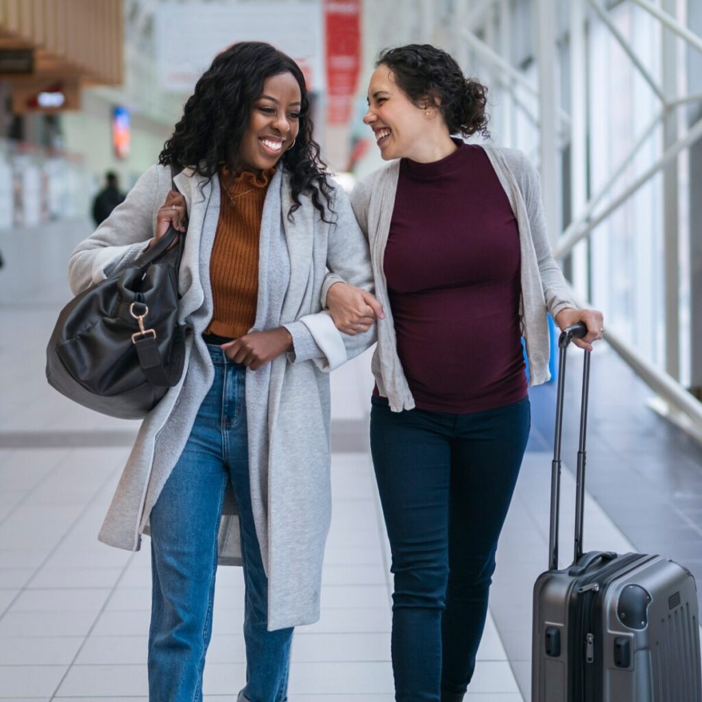Two women walking at the airport while carrying luggage.