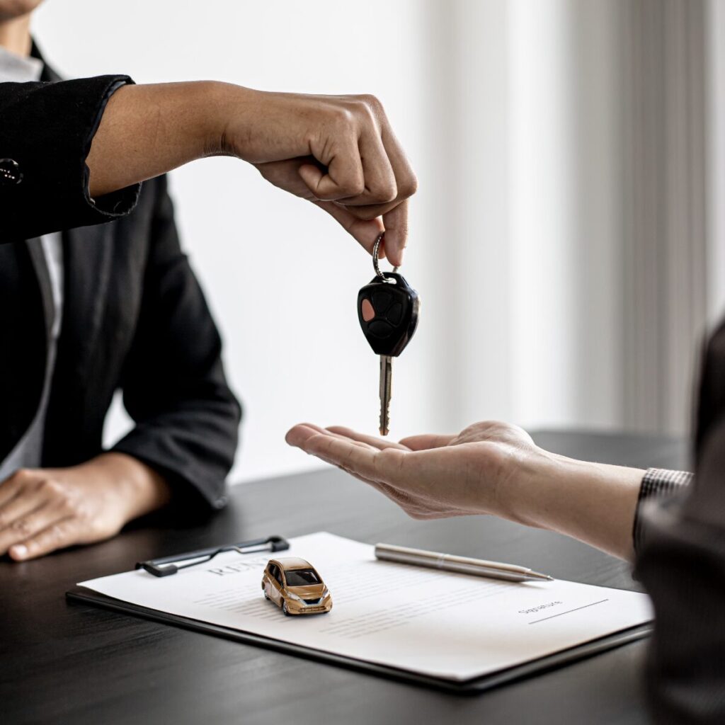 Person handing car key over, with car rental agreement on the table.